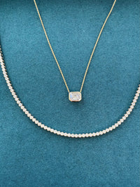 Gold necklace with a diamond pendant on a teal background