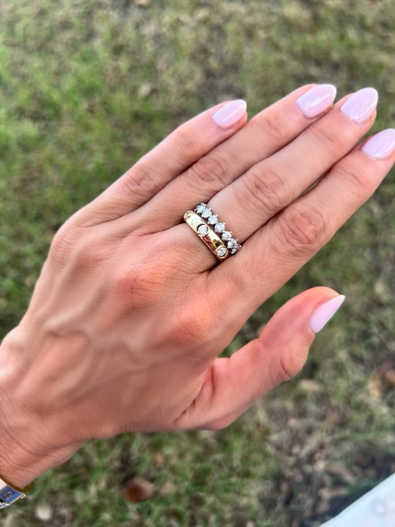Hand wearing a gold ring with gemstones against a blurred natural background