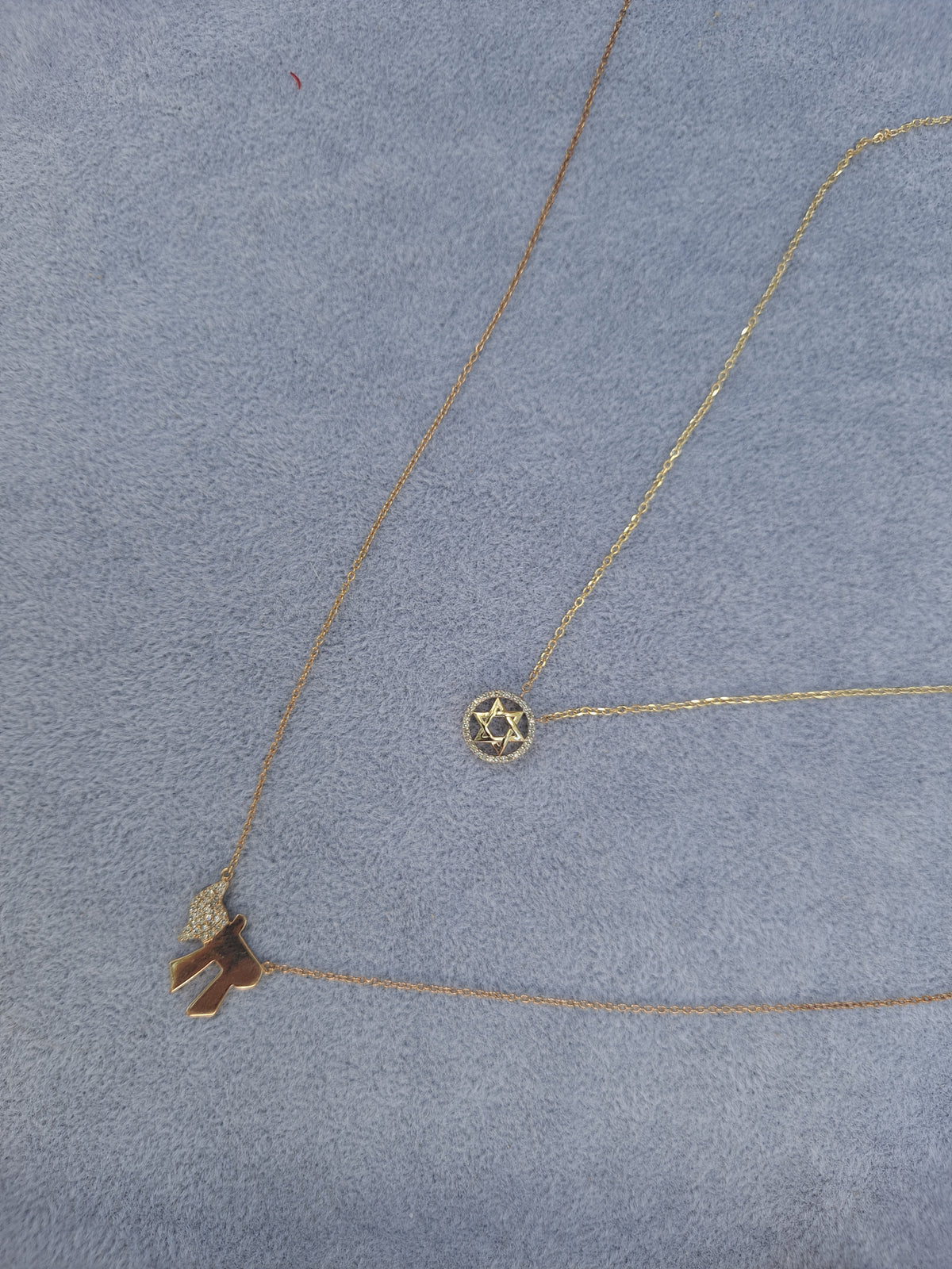 Two gold necklaces with pendants on a gray surface