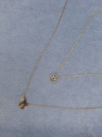 Two gold necklaces with pendants on a gray surface