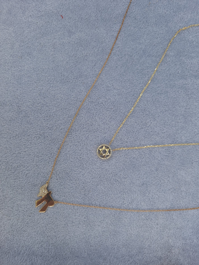Two gold necklaces with pendants on a gray surface