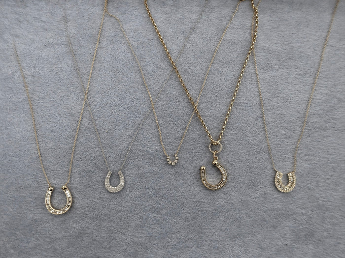 Four gold necklaces with horseshoe pendants on a gray surface