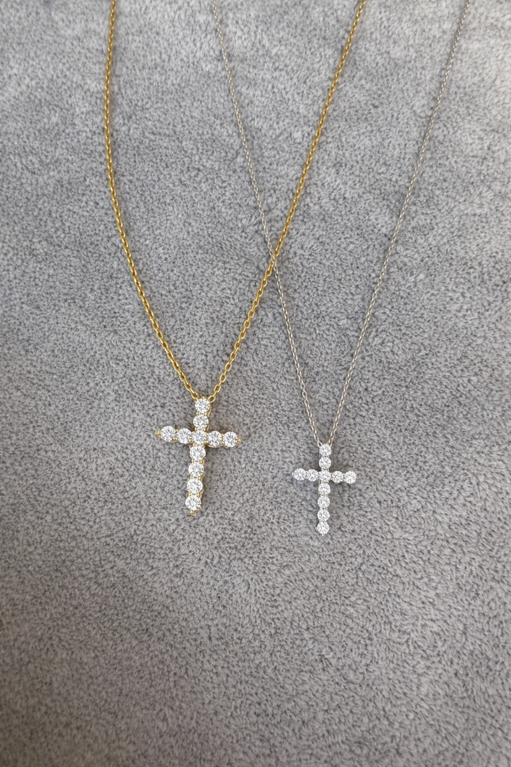 Two gold cross necklaces on a textured gray surface