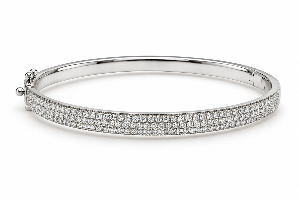 A polished silver-tone hinged bangle bracelet paved with small clear gemstones on the front band, shown on a clean white background.