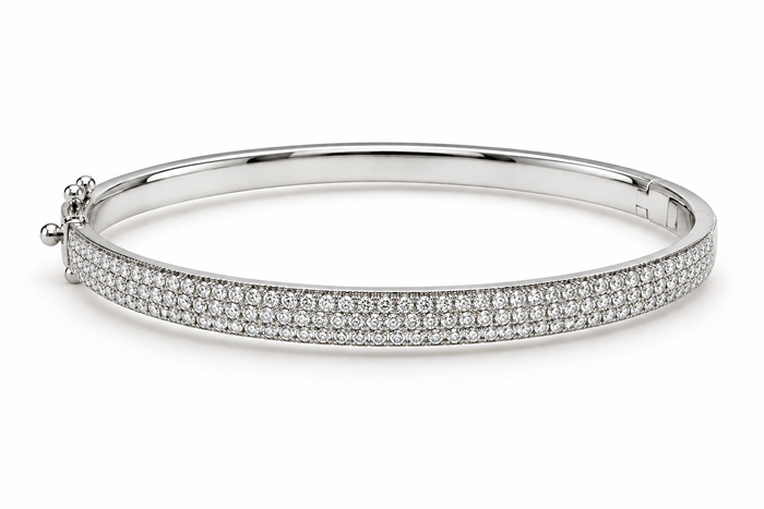 A polished silver-tone hinged bangle bracelet paved with small clear gemstones on the front band, shown on a clean white background.