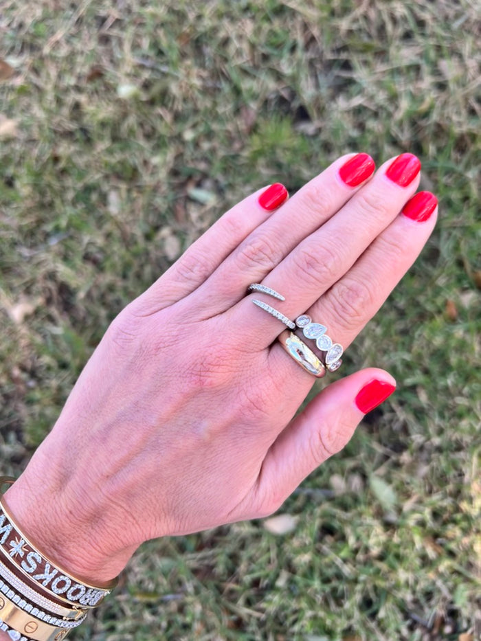 Hand with red nail polish wearing two silver rings against a grassy background