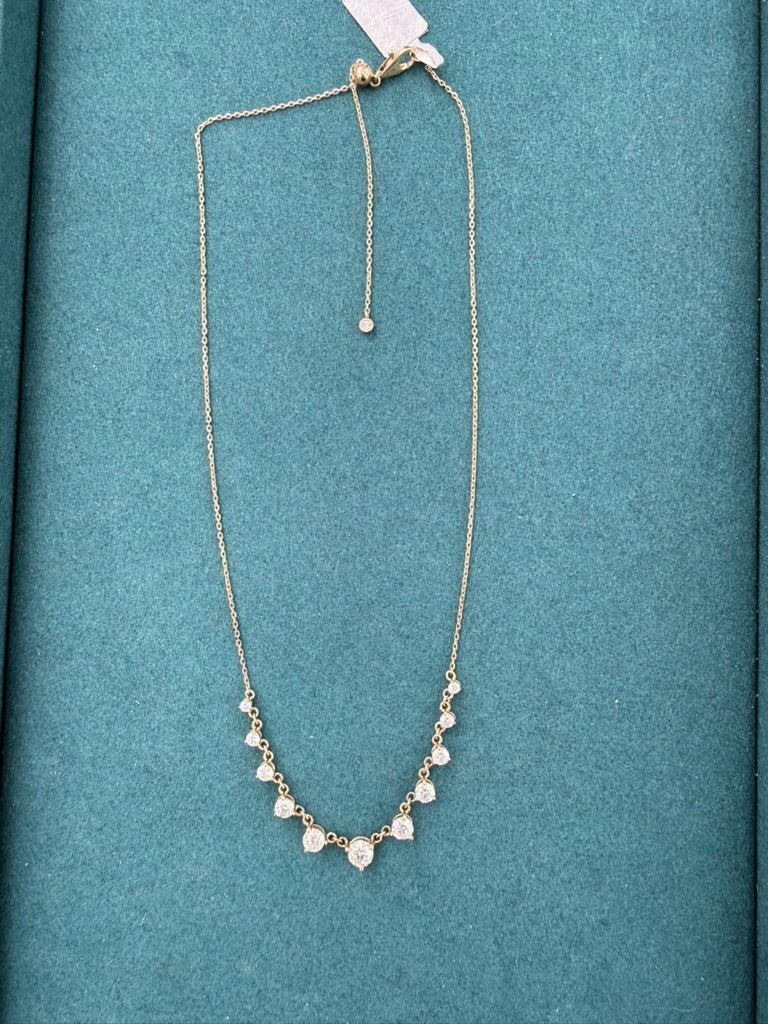 A delicate gold chain necklace with a V-shaped arrangement of small clear stones, displayed on a textured teal-blue background.