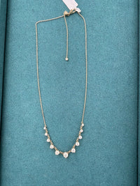 A delicate gold chain necklace with a V-shaped arrangement of small clear stones, displayed on a textured teal-blue background.