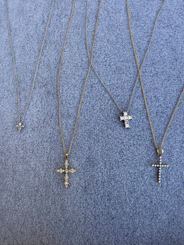 Four gold-tone cross pendant necklaces with varying diamond-studded cross pendants, laid out on a textured gray fabric background.