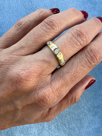 Gold ring with diamonds on a hand against a light blue background
