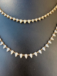 A gold-toned double-strand necklace featuring small teardrop-shaped pavé stone charms, displayed on a black textured surface.
