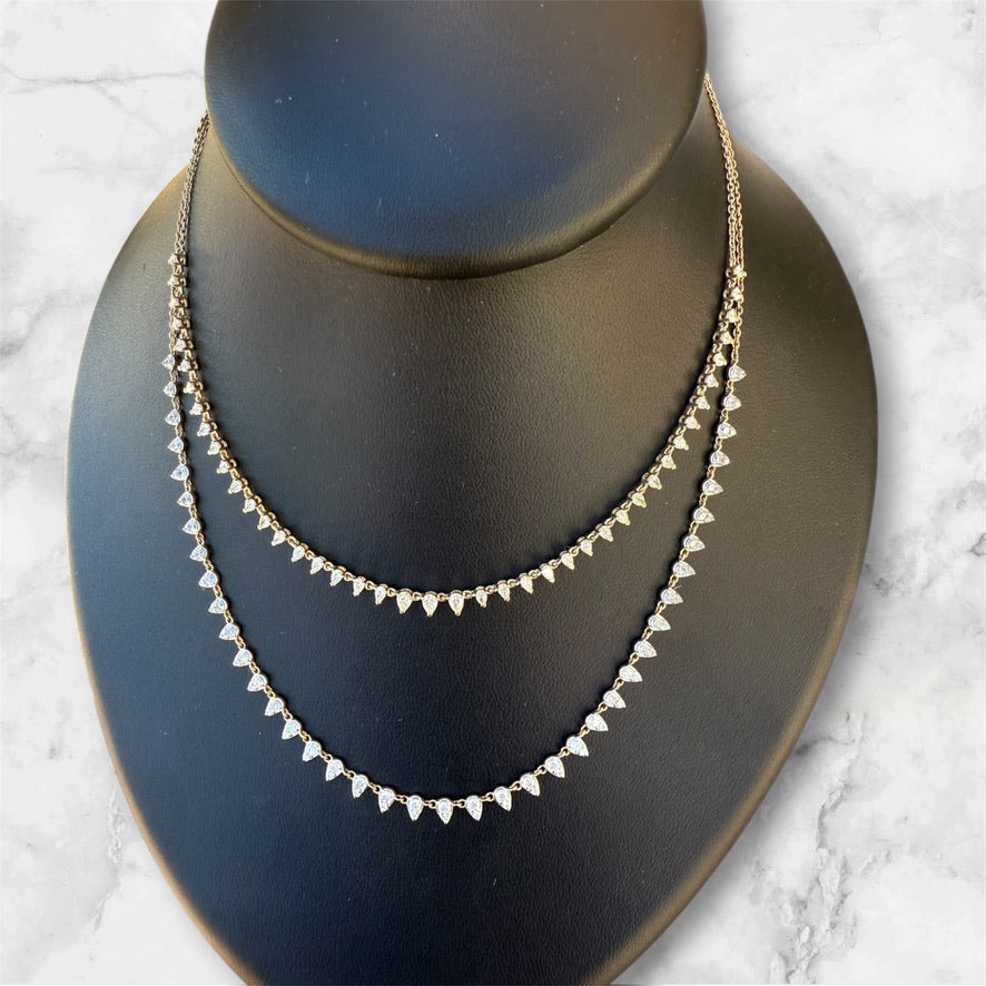 A double-strand gold necklace with small triangular clear stones, displayed on a black jewelry bust against a light marble background.
