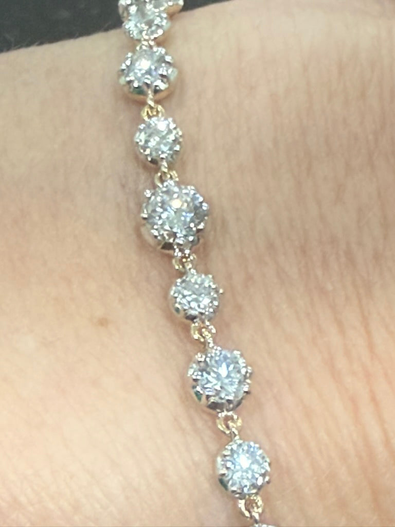 A close-up of a yellow gold tennis bracelet with round-cut clear gemstones set in a prong setting, worn on a person's wrist.