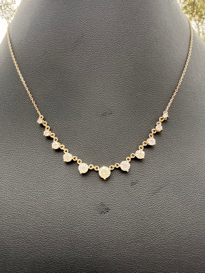 A delicate gold chain necklace with small heart-shaped gold pendants, each set with a clear round gemstone, displayed on a textured black jewelry bust.