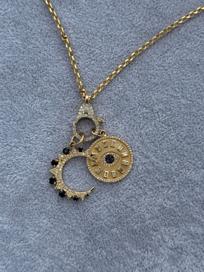 Gold necklace with a moon and evil eye pendant on a gray textured background