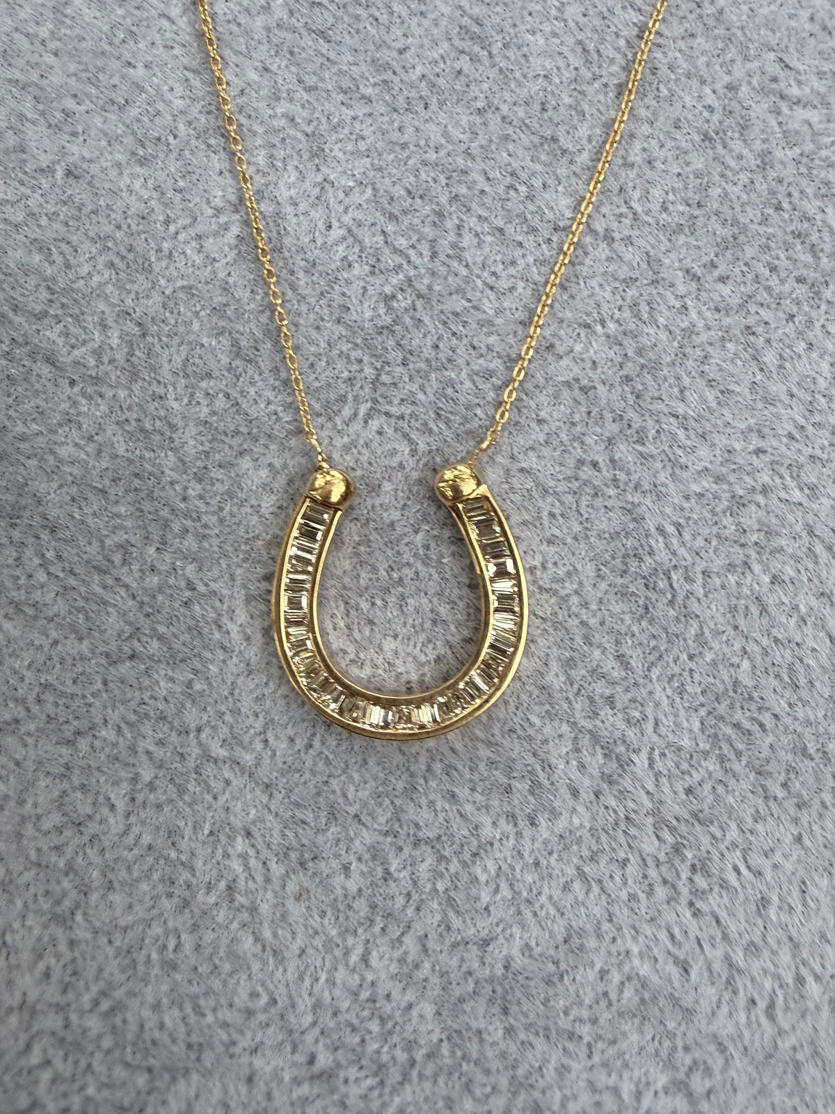 Gold horseshoe necklace on a gray textured background