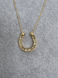 Gold horseshoe necklace on a gray textured background