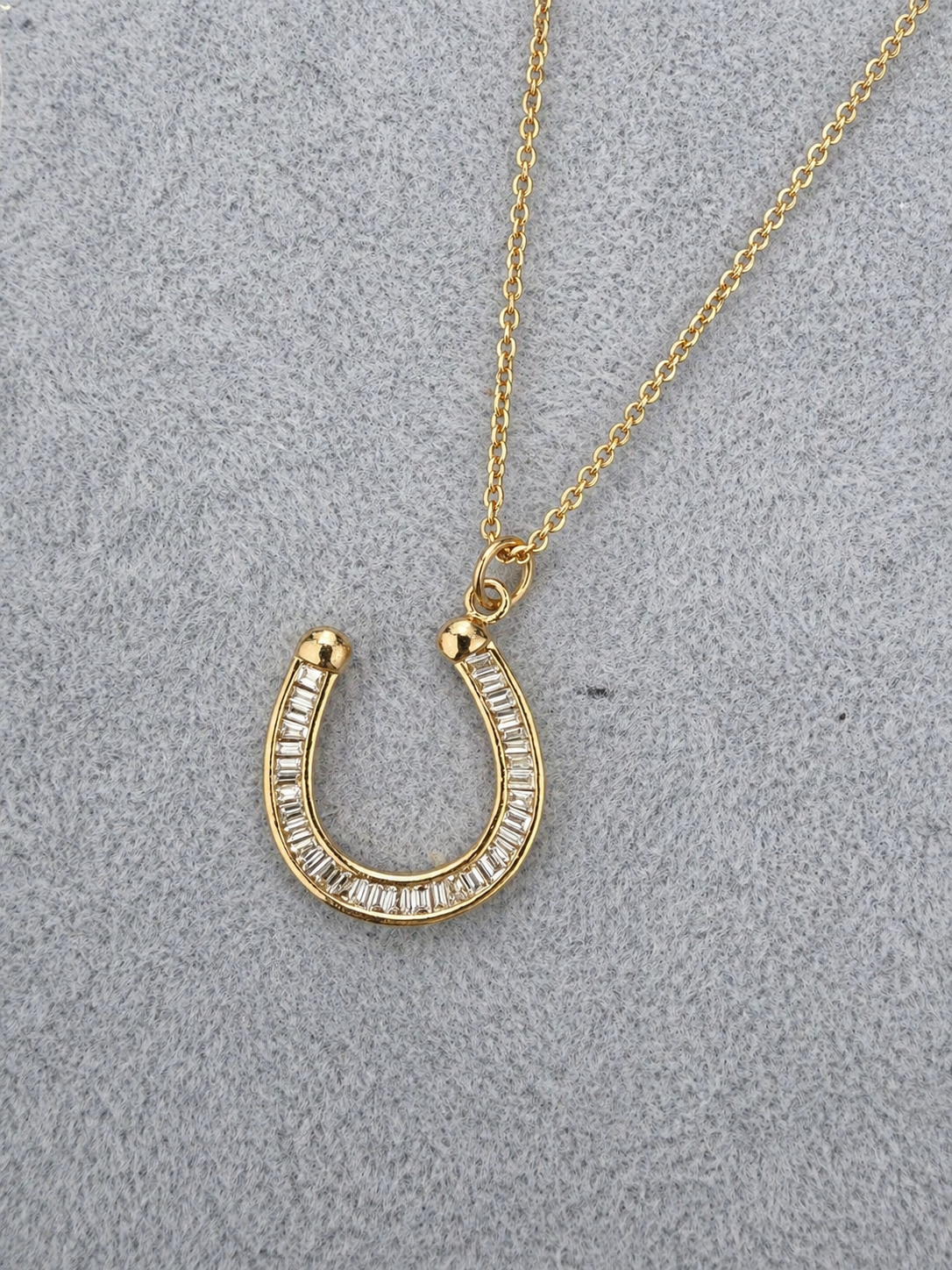 Gold horseshoe necklace with clear stones on a gray textured background