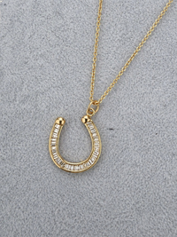 Gold horseshoe necklace with clear stones on a gray textured background