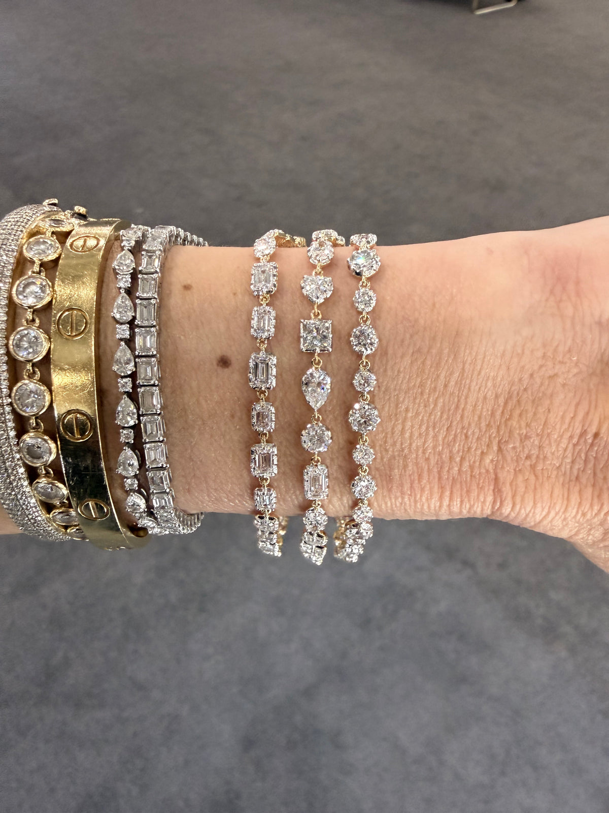 Close-up of a wrist wearing multiple diamond bracelets on a gray background