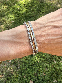 Close-up of a wrist wearing two gold bracelets with diamonds against a blurred green background