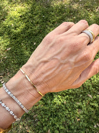 Hand wearing multiple bracelets and rings with a green outdoor background