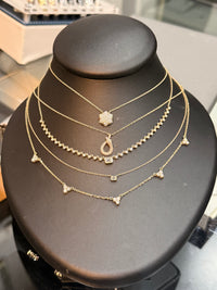 A multi-layered gold necklace set displayed on a black jewelry bust. The set includes a star-shaped pendant, a teardrop pendant, a beaded chain, a short chain with small triangular charms, and a short chain with a square charm.