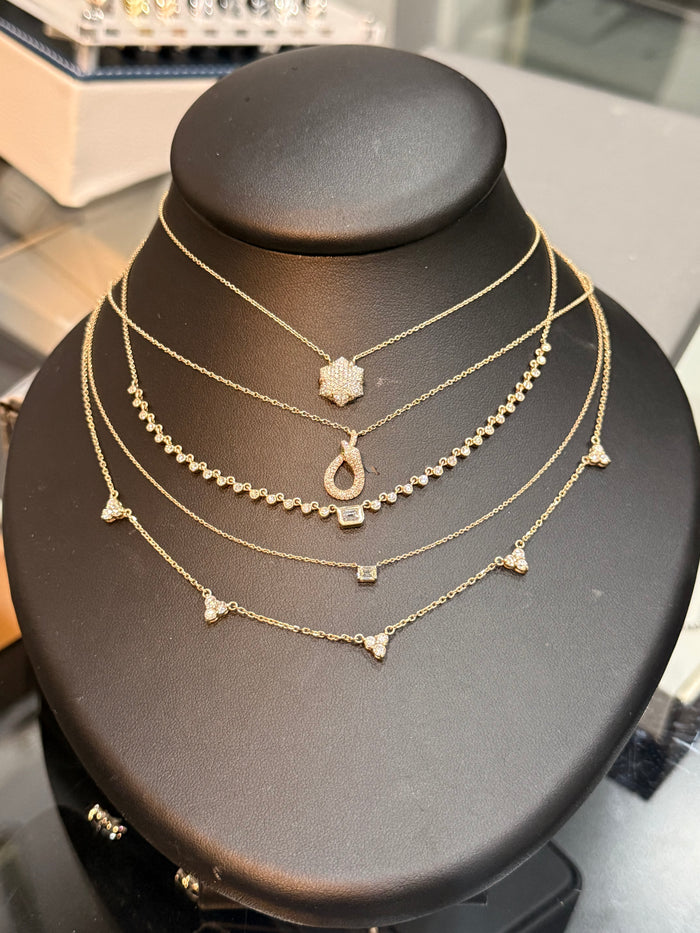 A multi-layered gold necklace set displayed on a black jewelry bust. The set includes a star-shaped pendant, a teardrop pendant, a beaded chain, a short chain with small triangular charms, and a short chain with a square charm.