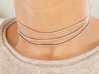 Close-up of a person wearing multiple tennis necklaces on a light background