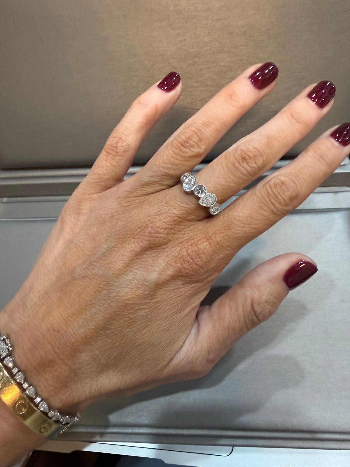 Hand wearing a silver ring with maroon nail polish on a neutral background