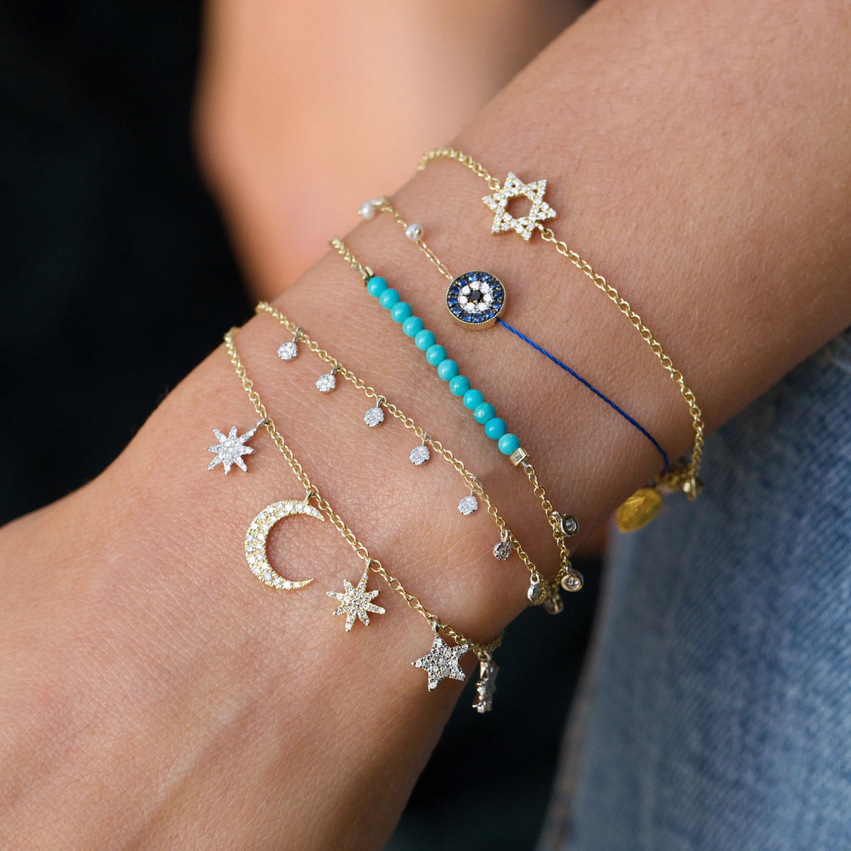 Close-up of a wrist wearing multiple gold bracelets with star, moon, and blue bead designs.