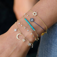Close-up of a wrist wearing multiple gold bracelets with star, moon, and blue bead designs.