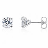 A pair of silver stud earrings, one shown from the front displaying a round brilliant-cut clear gemstone and the other from the side displaying the triangular prong setting and post with butterfly back, on a white background with a soft reflection.