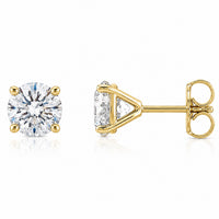 A pair of yellow gold stud earrings, one shown from the front with a round brilliant-cut clear gemstone and the other from the side showing the triangular prong setting and post with butterfly back, on a white background.