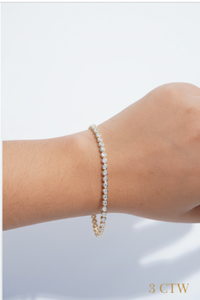 A delicate tennis bracelet with small diamonds set in a gold-tone band, shown worn on a person's wrist against a clean white background.