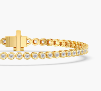 A gold tennis bracelet with a cross clasp and a continuous row of round-cut clear stones, shown on a clean white background.