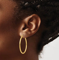 The Karat Concierge 1.5 inch 14K yellow gold hoop earrings worn on a model's ear, showcasing a polished finish.