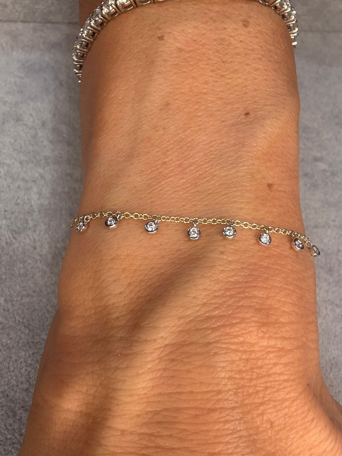 The Karat Concierge 14k yellow gold dangle bracelet with nine bezel-set diamonds worn on a wrist.