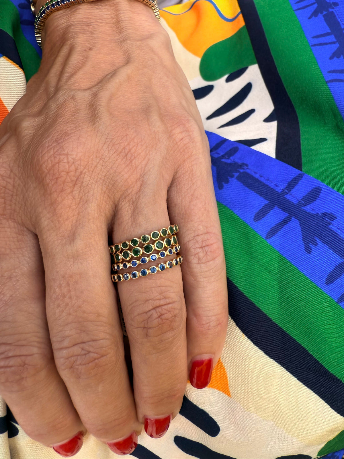 The Karat Concierge 14K yellow gold eternity bands featuring bezel-set emerald and sapphire gemstones on a hand.