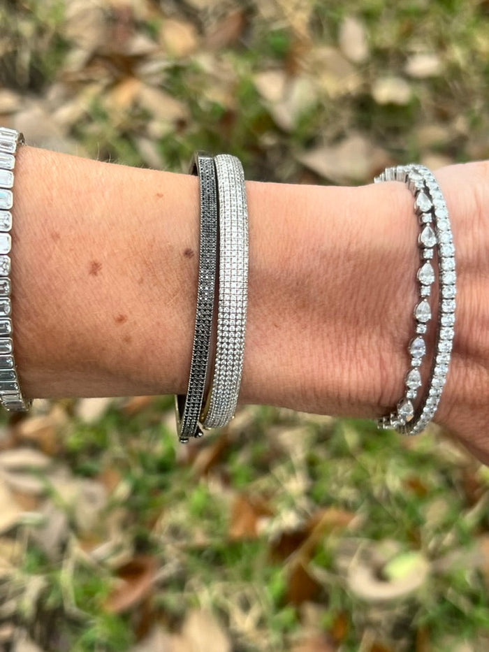 The Karat Concierge black diamond pave bangle in black rhodium worn on a wrist with other diamond bracelets.