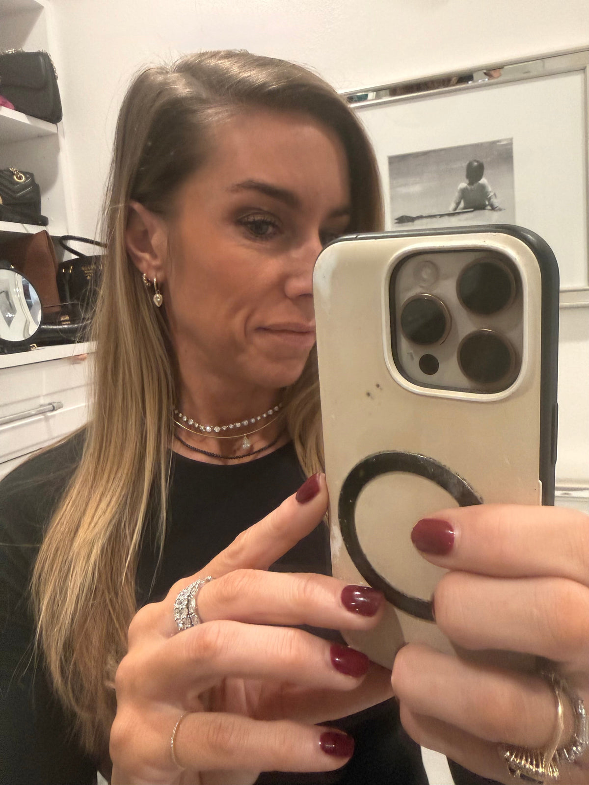 The Karat Concierge black diamond beaded necklace layered with gold chains on a woman taking a mirror selfie