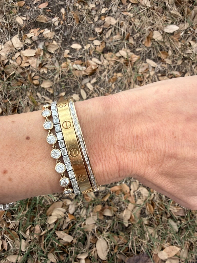 The Karat Concierge channel set baguette diamond bangle worn on a wrist with other gold and diamond bracelets.