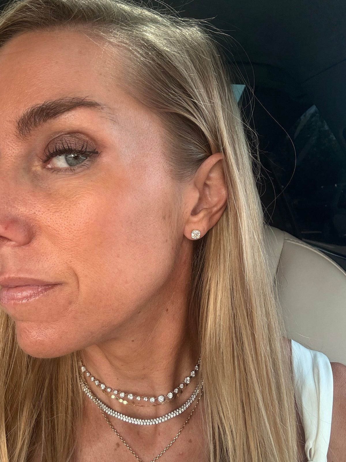 The Karat Concierge cushion cut diamond stud earrings in 18K yellow gold worn by a woman with blonde hair