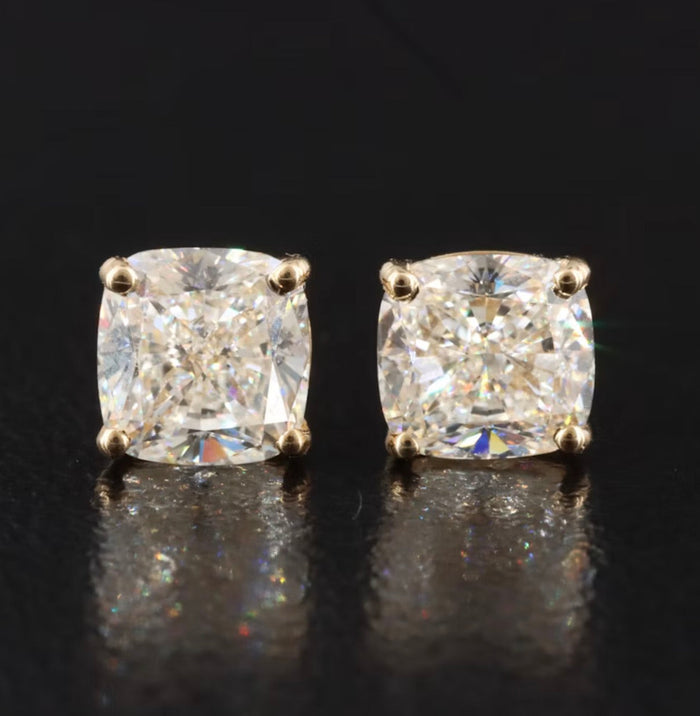 The Karat Concierge 2.08 CTW cushion cut diamond stud earrings set in 18K yellow gold on a black reflective surface.