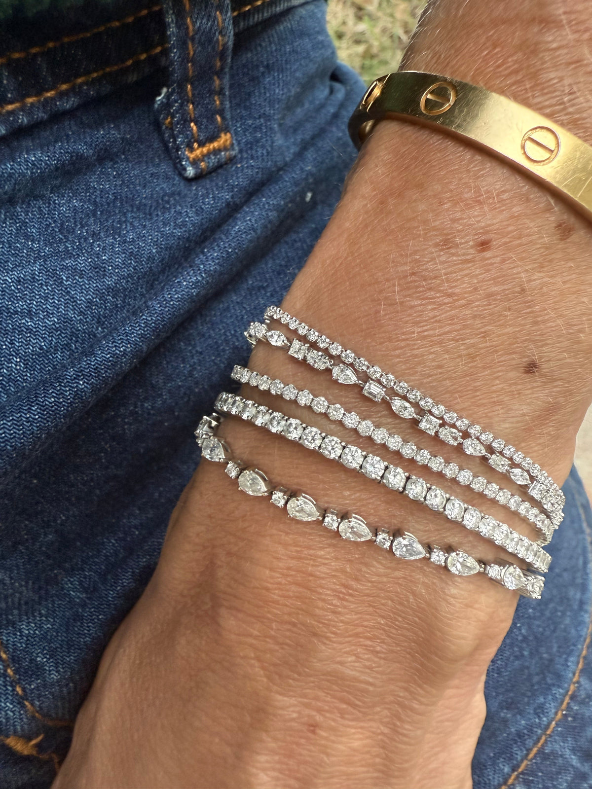 The Karat Concierge diamond tennis bracelets in 14K white gold worn stacked on a wrist with denim and a gold bangle.