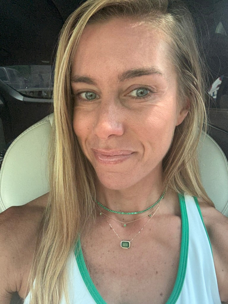 The Karat Concierge emerald bezel set necklace in 14K yellow gold worn by a woman with a green and white top.