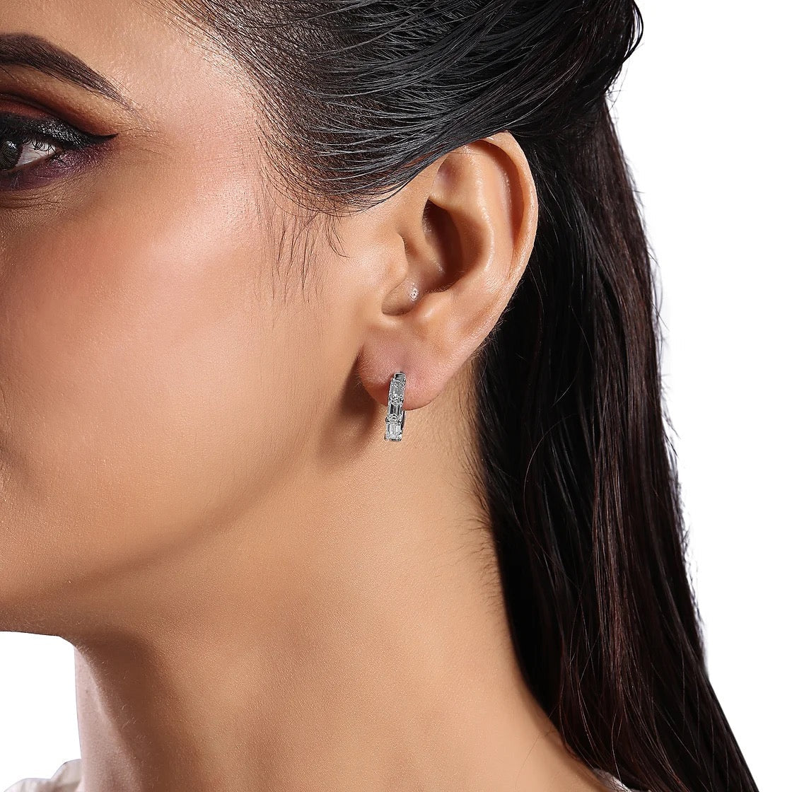 The Karat Concierge 14K white gold huggie earrings featuring three emerald cut diamonds worn on a model's ear