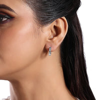 The Karat Concierge 14K white gold huggie earrings featuring three emerald cut diamonds worn on a model's ear