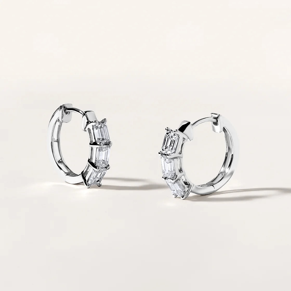 The Karat Concierge 14K white gold huggie earrings featuring three emerald cut diamonds on each hoop.