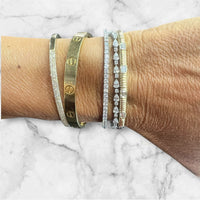 The Karat Concierge emerald cut fluted diamond bangle worn on a wrist with stacked gold and diamond bracelets.